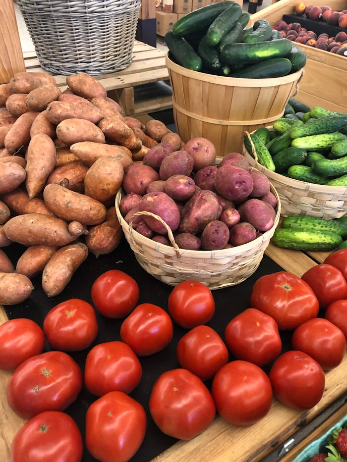 Fresh tomatoes, sweet potatoes, cucumbers, and potatoes on display at a market.